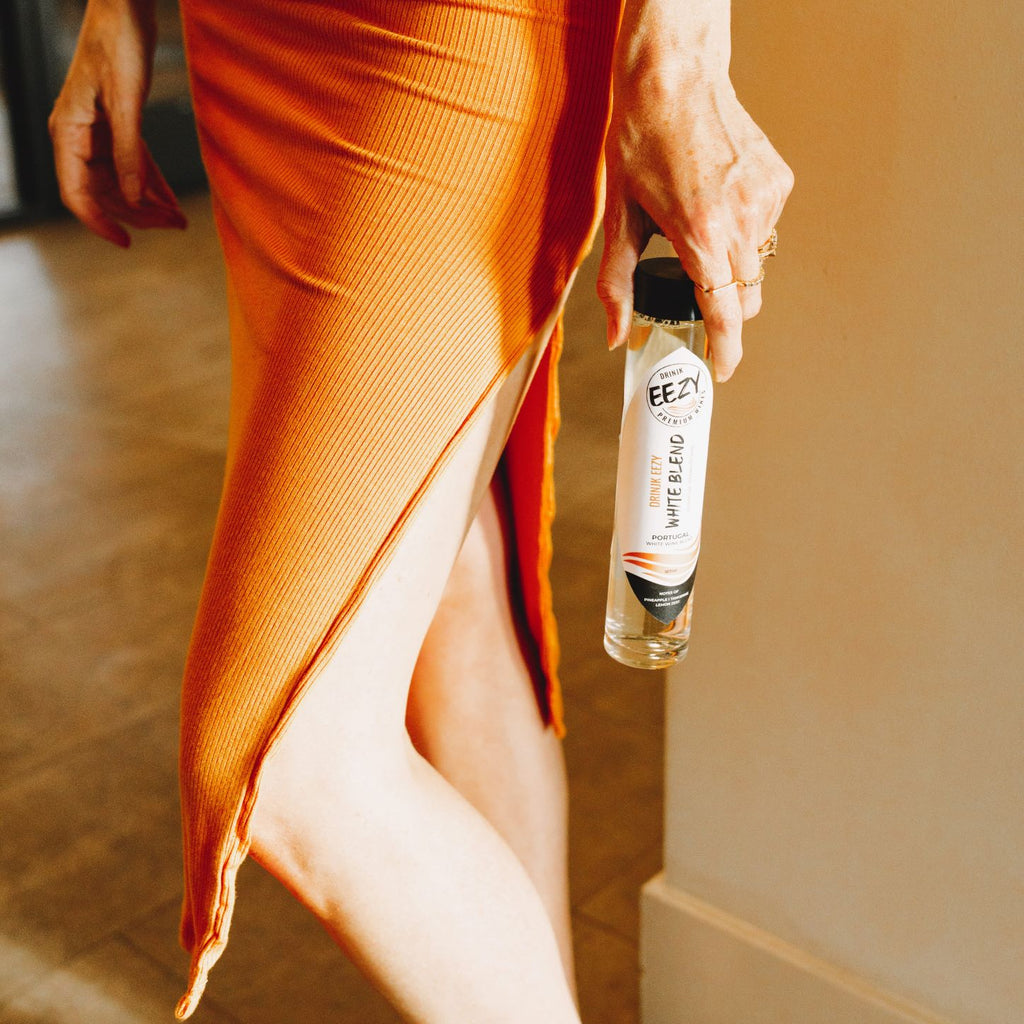A Girl in an orange dress holding a Drink EEZY SIngle-Serve Wine from the Wine Membership